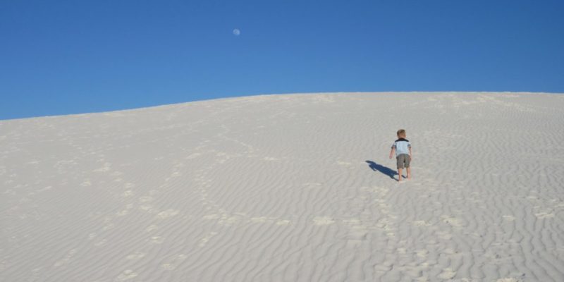 child climbs large sand dune at White Sands National Monument in New Mexico