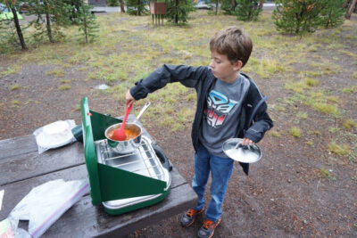 boy cooks over camp stove