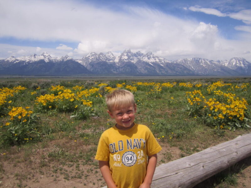 boy with wildflowers and mountains in background in Grand Teton National Park